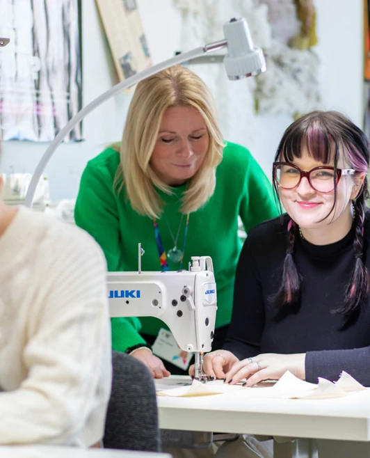 A fashion lecturer assisting students with their sewing projects in the design workshop. A fashion lecturer assisting students with their sewing projects in the design workshop.